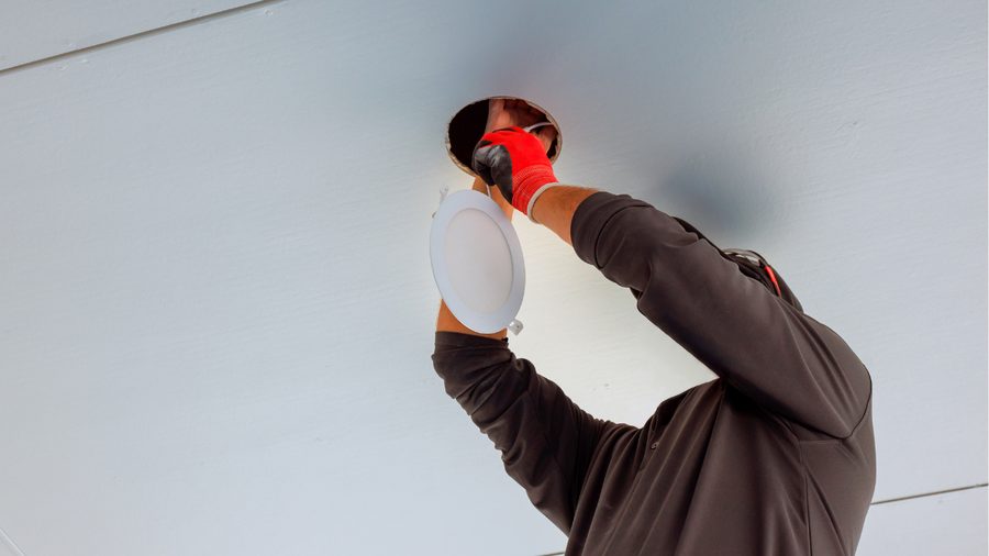 Technician installing a recessed ceiling light during an overnight relamping visit