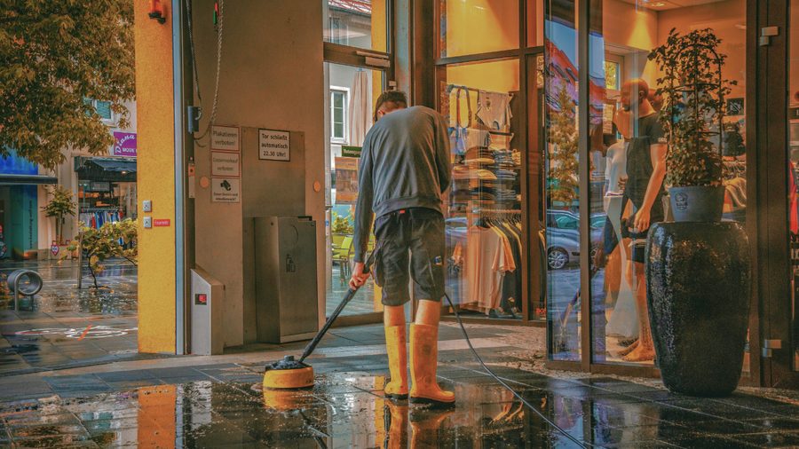 Operative pressure-washing a retail storefront entrance before opening